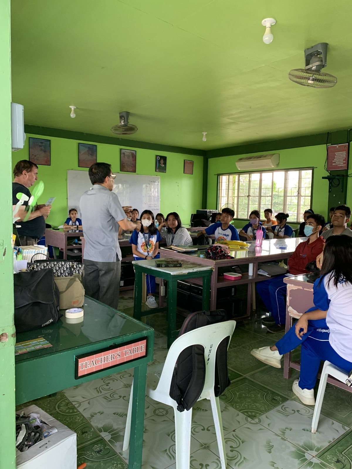 A Filipino pastor preaching to students inside a green-walled public school classroom