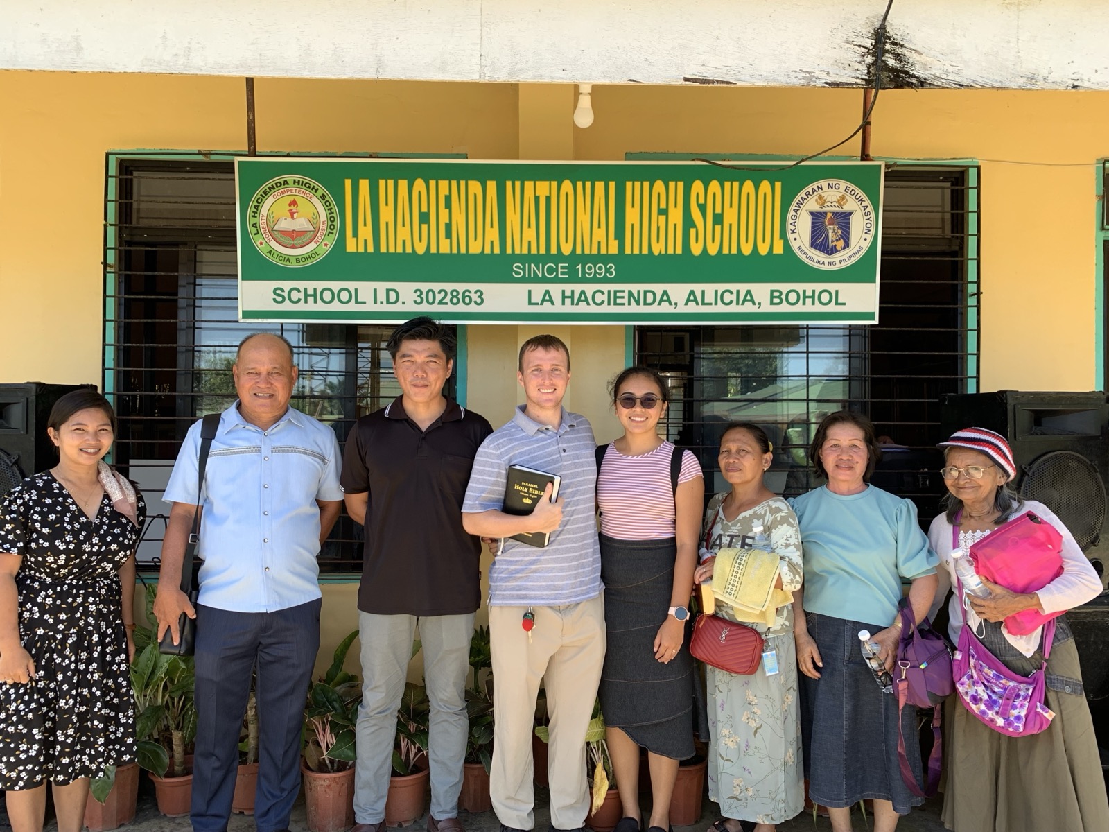 The Schneide team standing under the La Hacienda National High School banner with church members