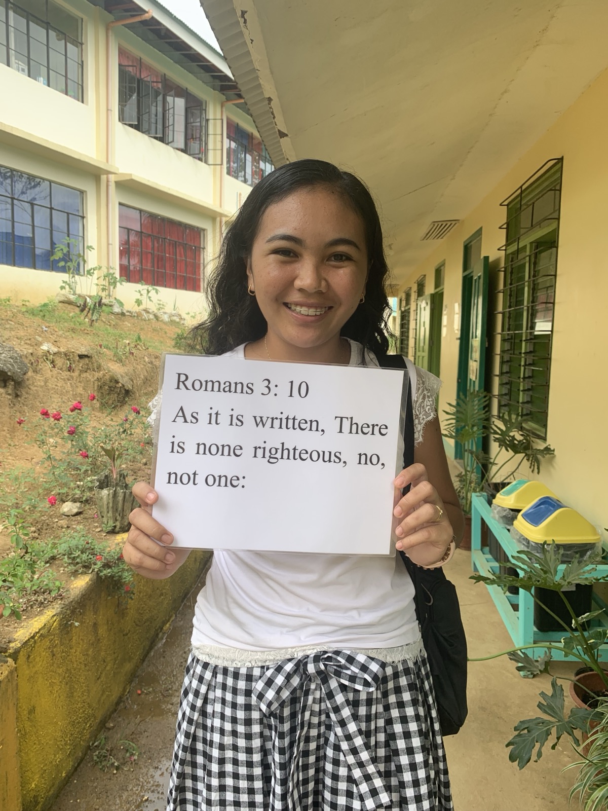 A young Filipino woman holding a verse card showing Romans 3:10